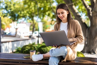 En tjej som jobbar på en laptop utomhus under ett träd