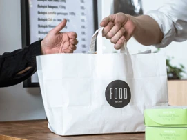 Cashiers hand over a paper bag of take-away food to customers.