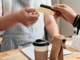 The customer hands over membership cards to the cashier. A coffee and a paper bag are on the cash counter.